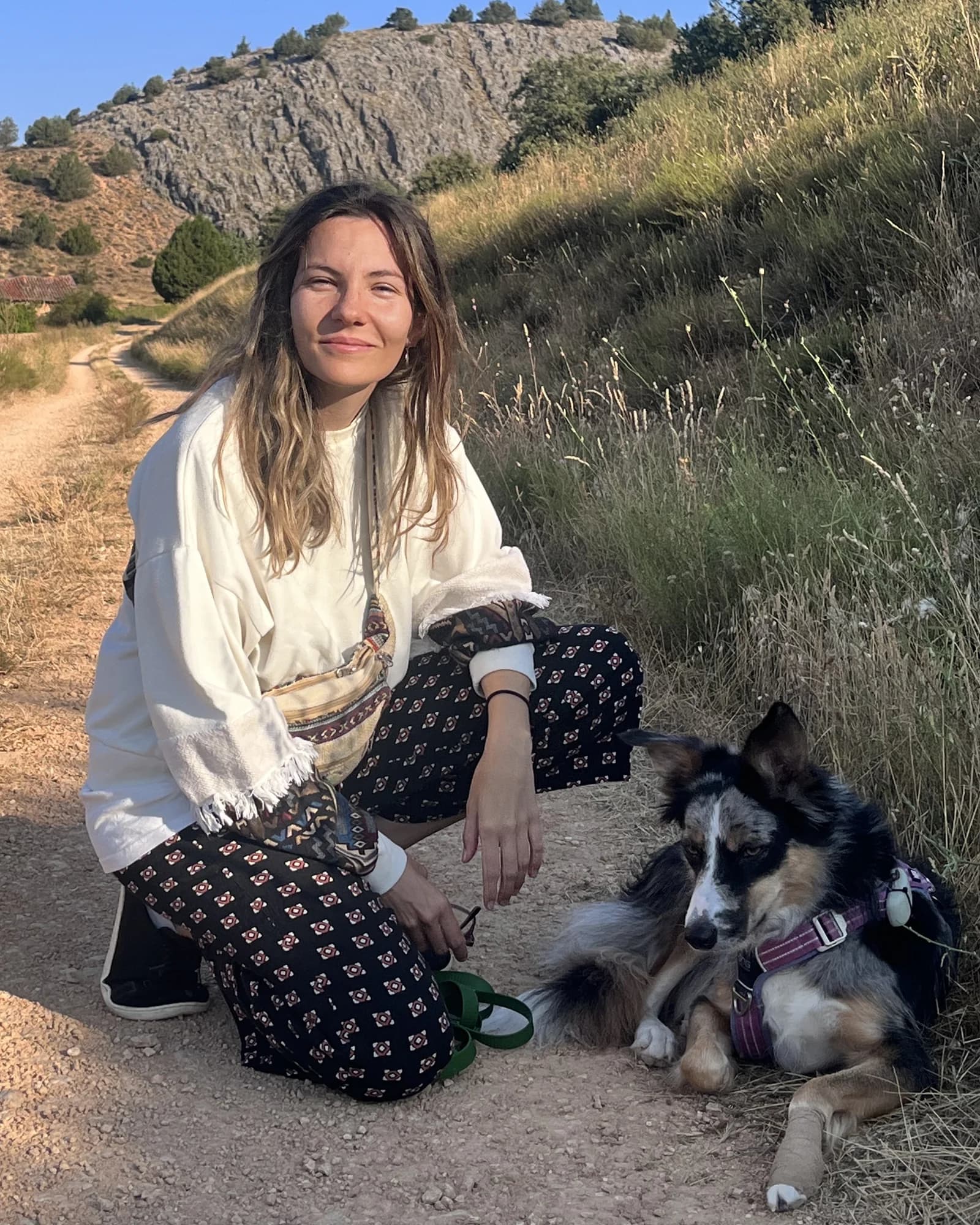 Sandra, sonriente, agachada en un camino de tierra junto a Area, su border collie